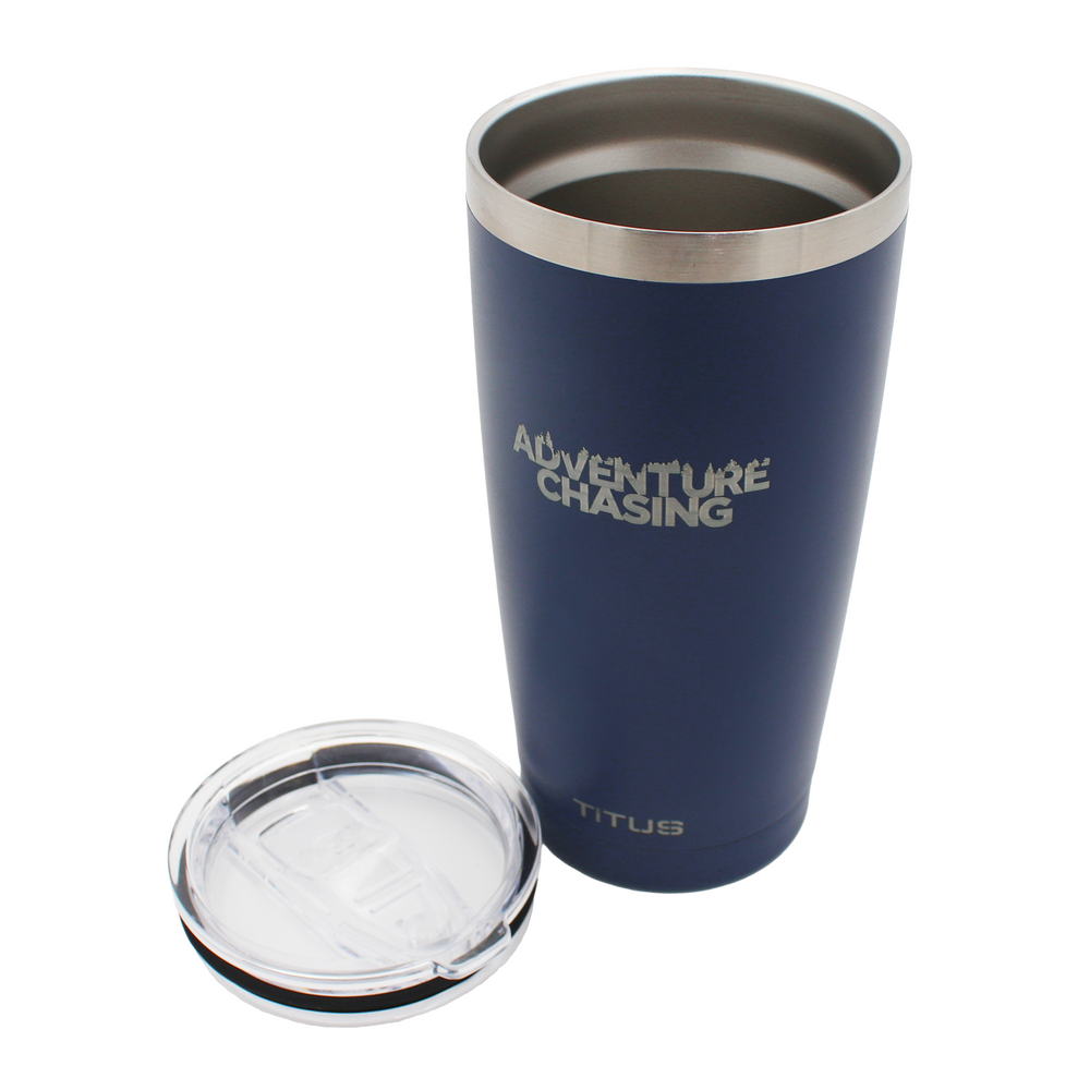 Navy blue tumbler with silver engraved 'Adventure Chasing' text on it and a clear plastic lid resting next to it.