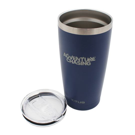 Navy blue tumbler with silver engraved 'Adventure Chasing' text on it and a clear plastic lid resting next to it.