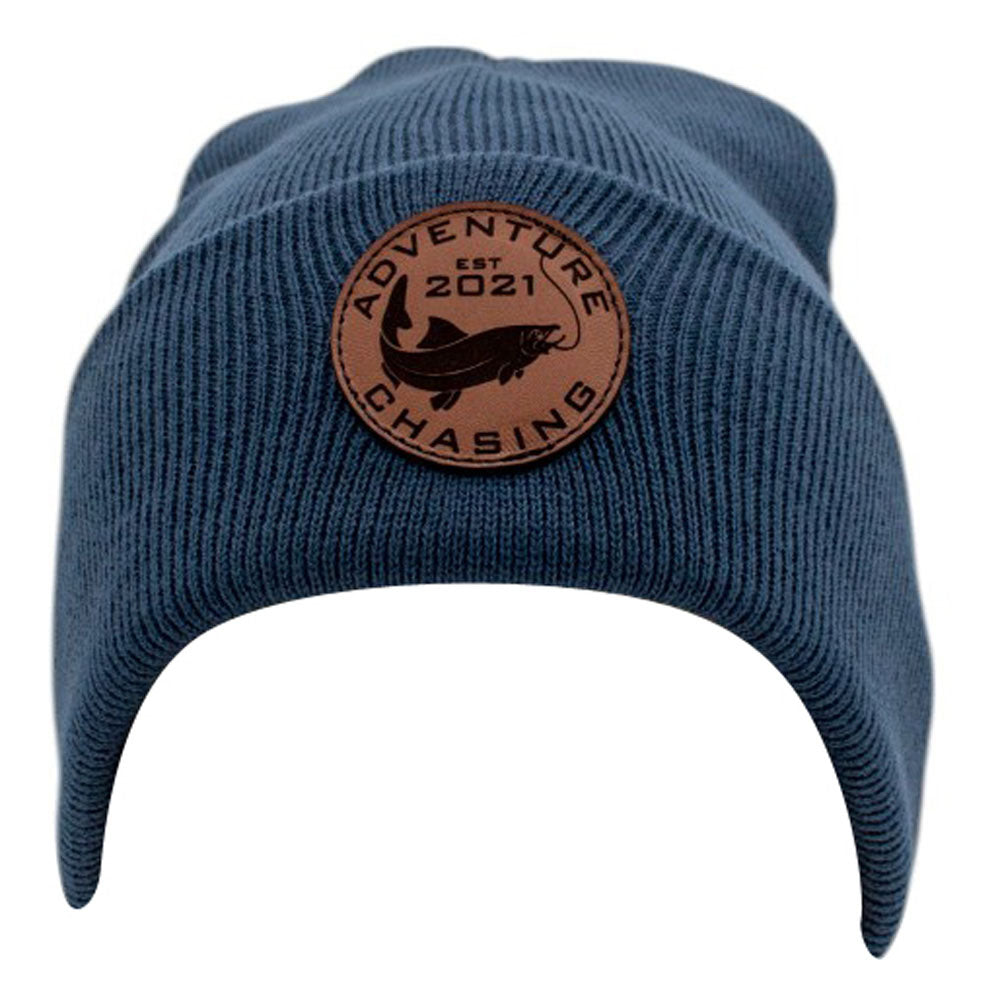 Navy beanie hat with a round leather patch featuring the text 'Adventure Chasing EST 2021'.