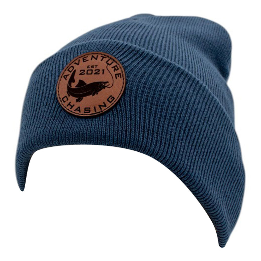 Blue knitted beanie hat with a brown leather patch featuring the text 'Adventure Chasing EST 2021'.